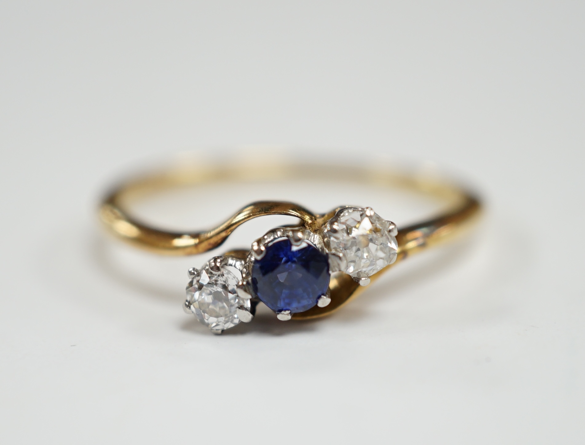An 18ct, single stone sapphire and two stone diamond set crossover ring, size O, gross weight 2.2 grams.